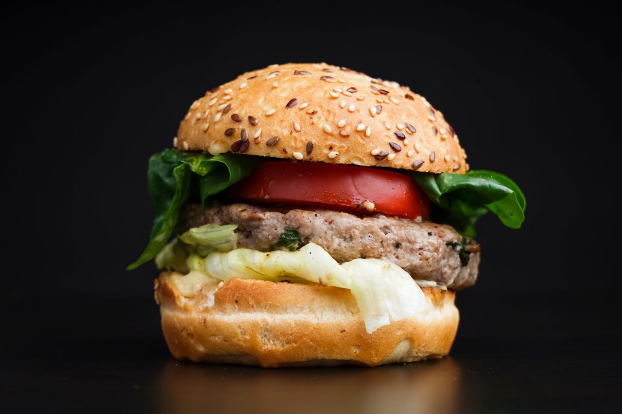 Close-up of a delicious burger with lettuce, tomato, and sesame seed bun on black background.