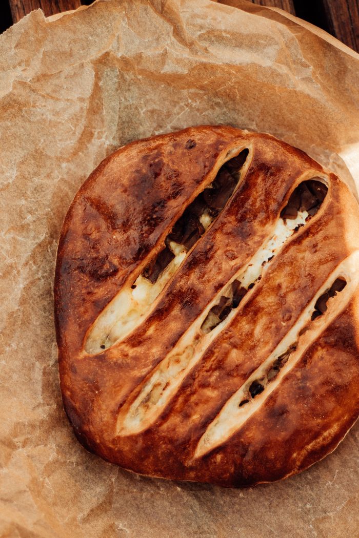 Artisan bread loaf with slits on baking paper, showcasing crispy crust.